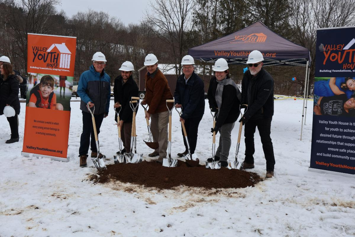 A group of people in hard hats shoveling dirt in the snow Description automatically generated